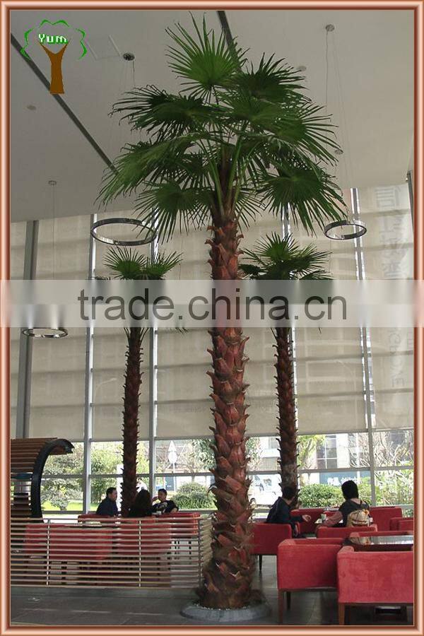 Big artificial palm tree with fan shape palm branches and real palm bark