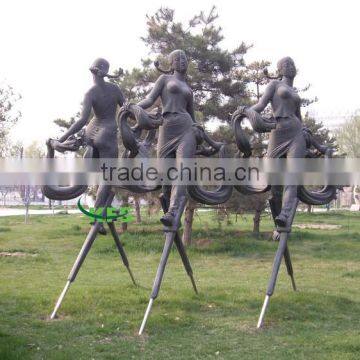 Bronze ladies walking on stilts outdoor statue