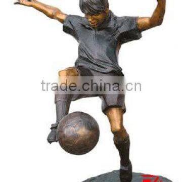 Bronze guy sculpture playing a football In garden